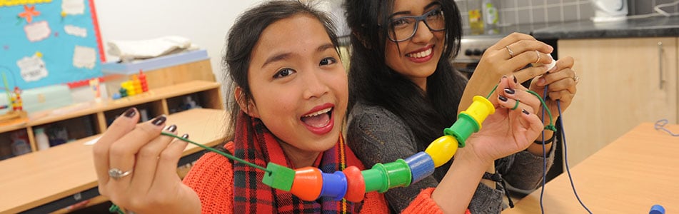Early years students with cotton reels on string